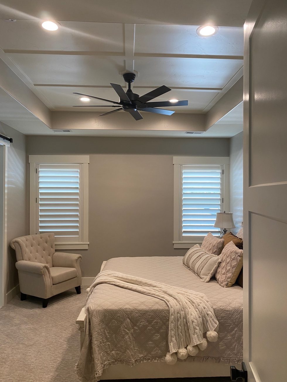 Bedroom with custom wall paneling, tray ceiling, and plantation shutters