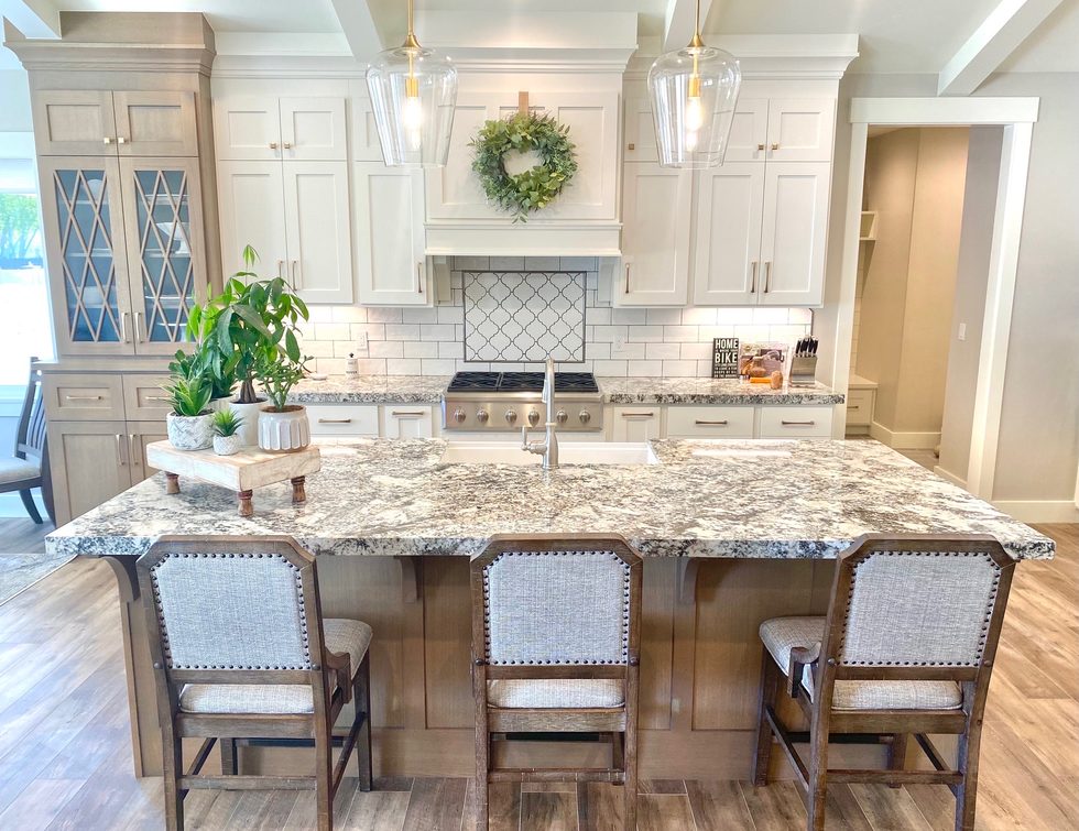White kitchen with granite island, upholstered bar stools, and glass-front cabinets