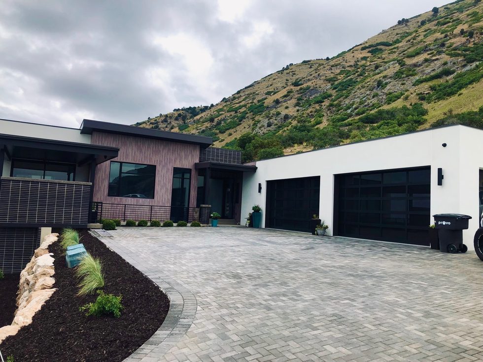 Modern dark-and-white custom home with a paver driveway at the base of the mountain