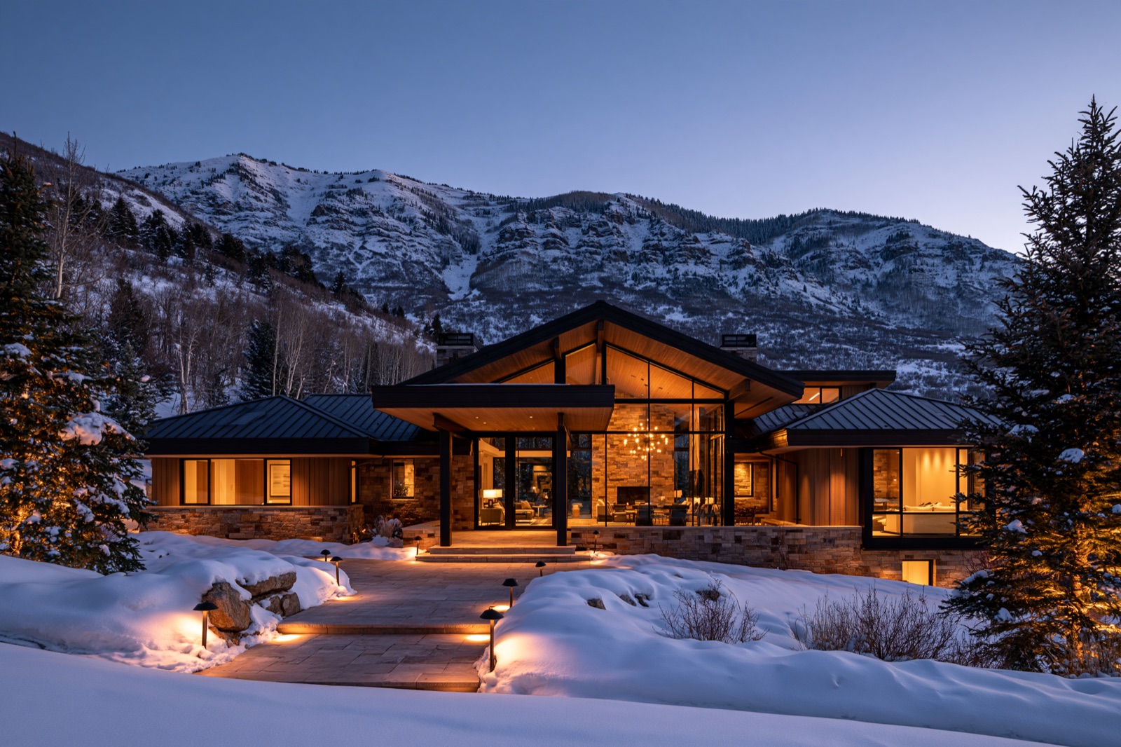 Modern mountain home with warm windows lit at dusk in snow