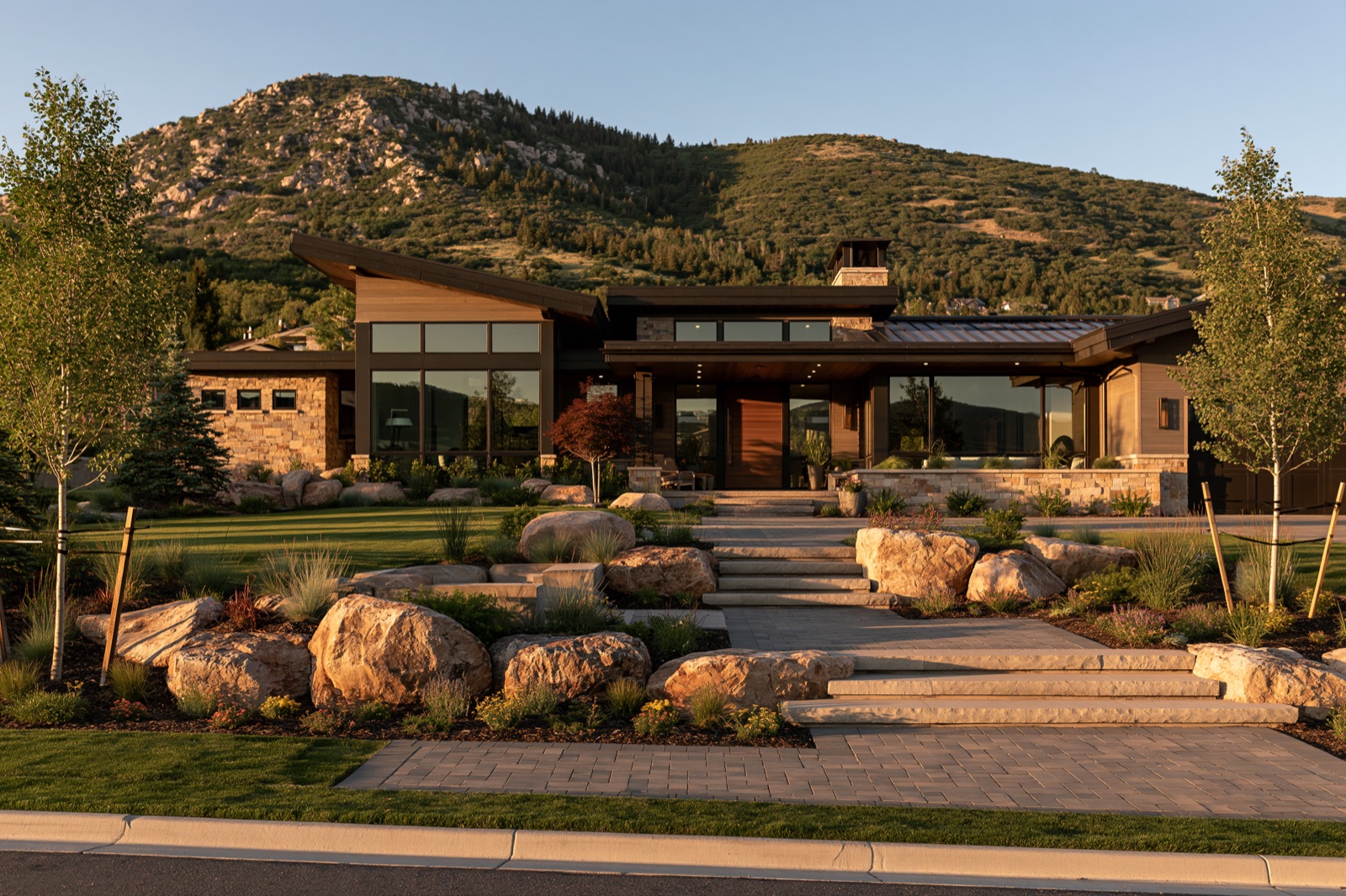 Finished modern mountain home with native landscaping, boulders, and a paver driveway